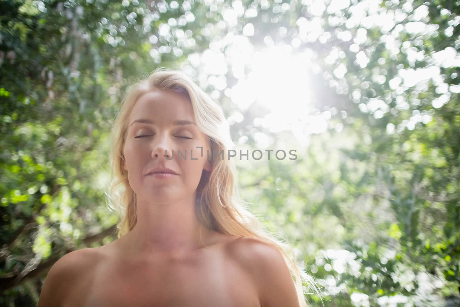 Beautiful woman meditating against bright sunlight in park