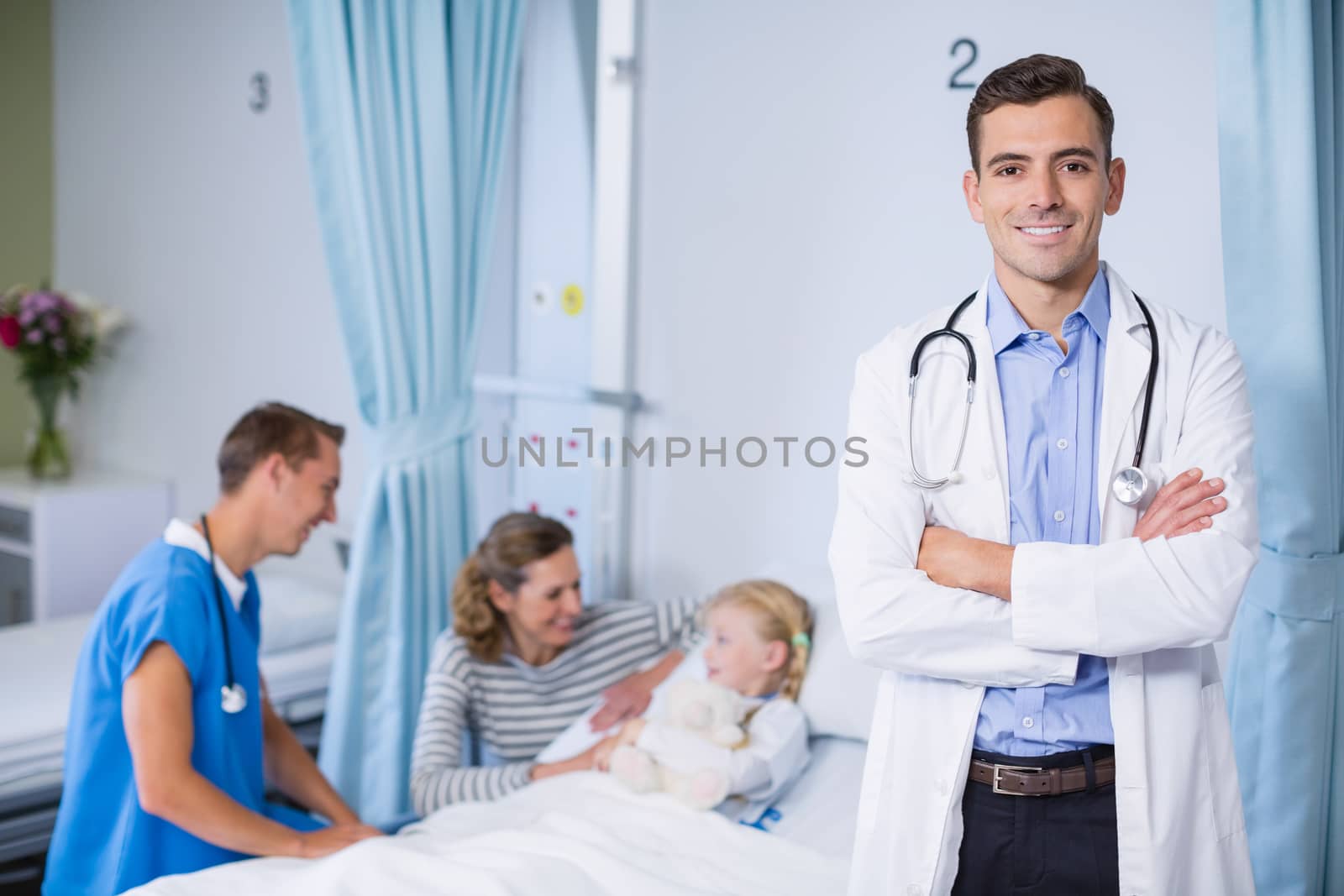 Portrait of smiling doctor standing with arms crossed in hospital bed