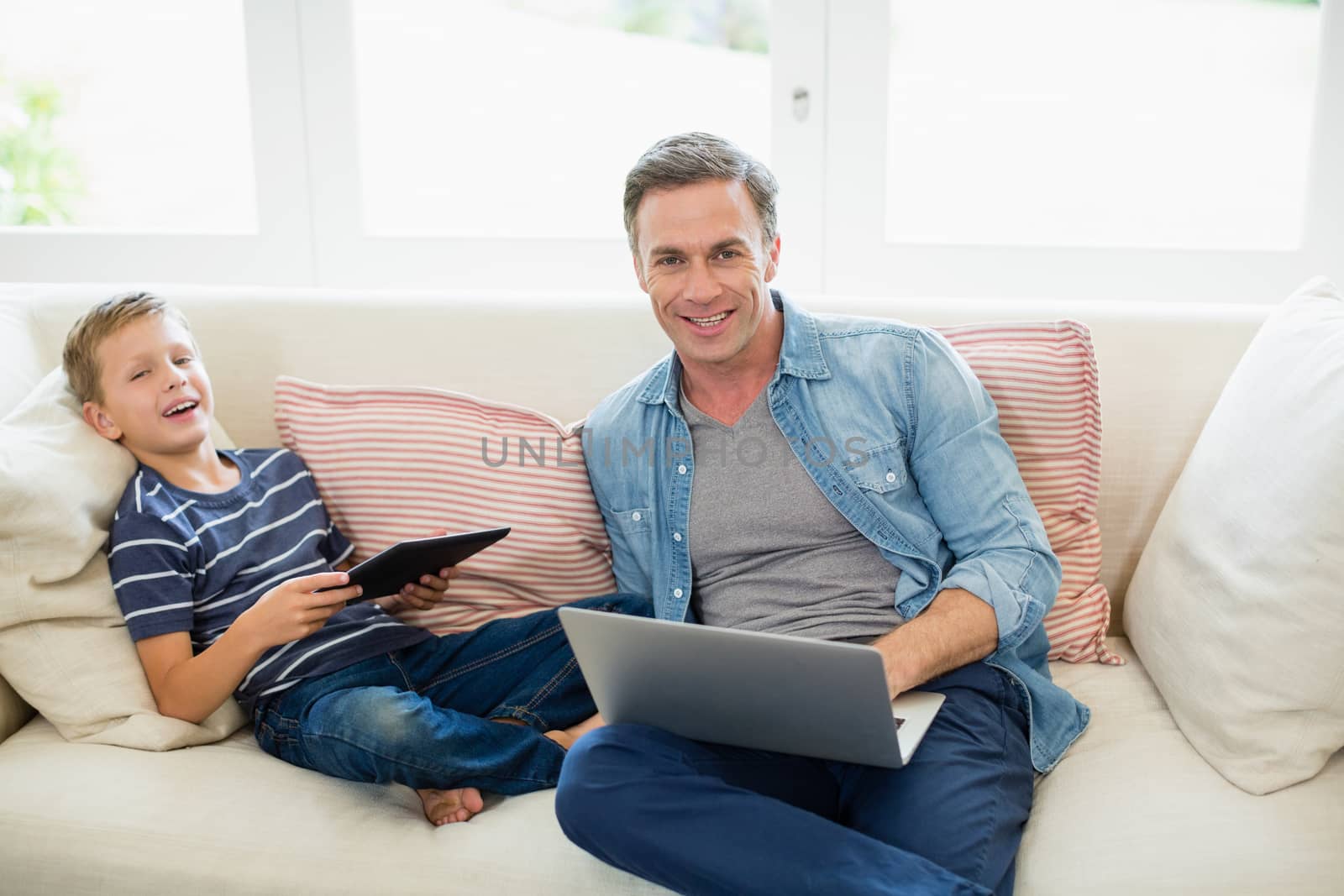 Portrait of father and son using laptop and digital tablet in living room at home