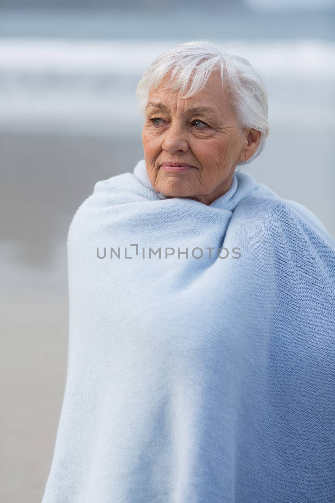Thoughtful senior woman wrapped in shawl on the beach