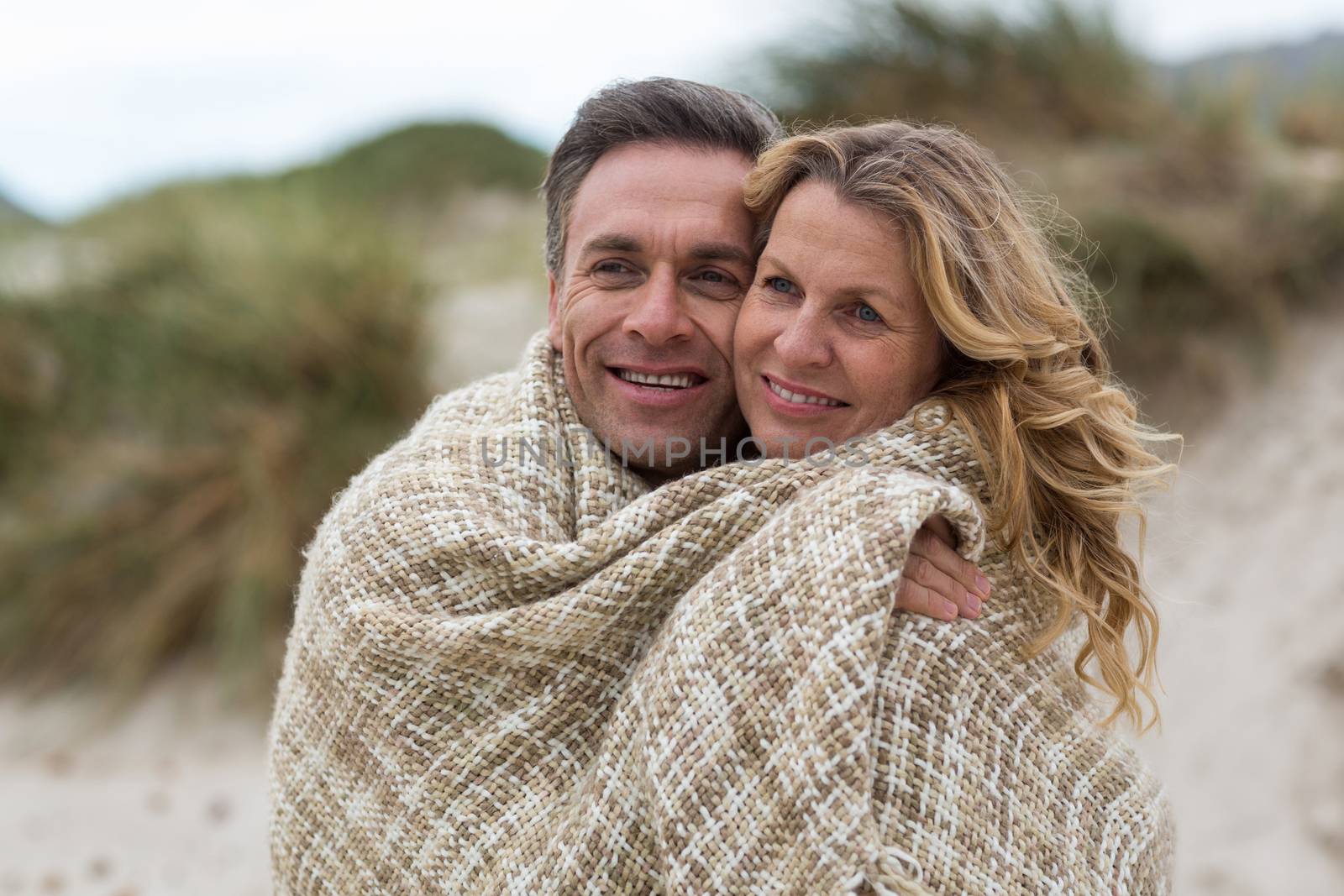 Mature couple wrapped in blanket on the beach by Wavebreakmedia