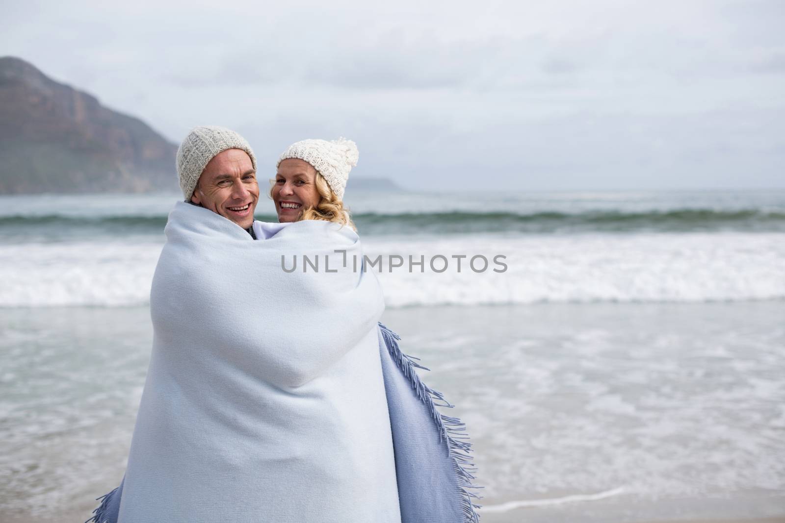 Mature couple wrapped in blanket on the beach by Wavebreakmedia