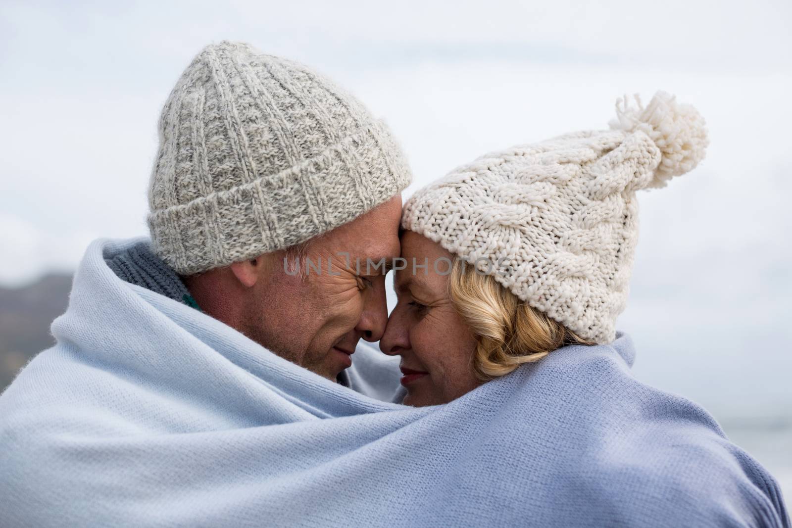 Mature couple wrapped in blanket on the beach by Wavebreakmedia