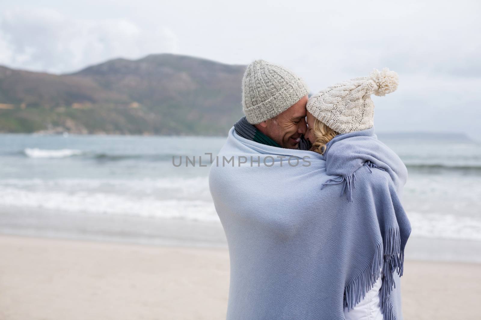 Mature couple wrapped in blanket on the beach by Wavebreakmedia