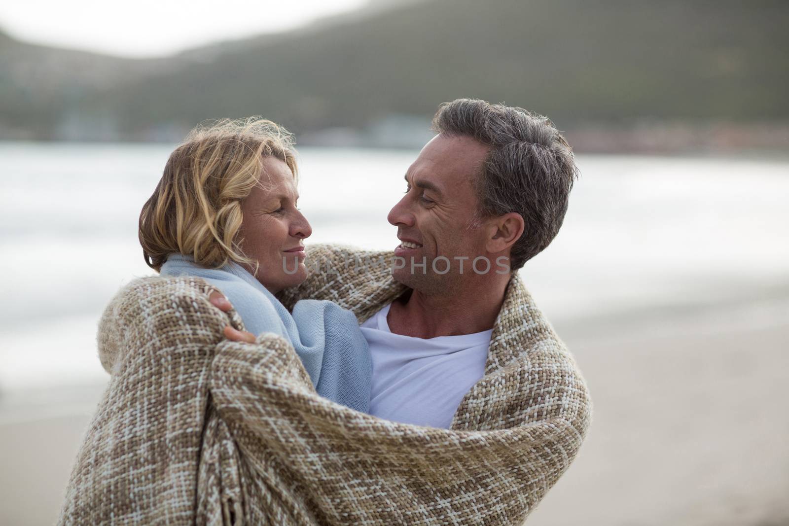 Romantic mature couple wrapped in blanket on the beach