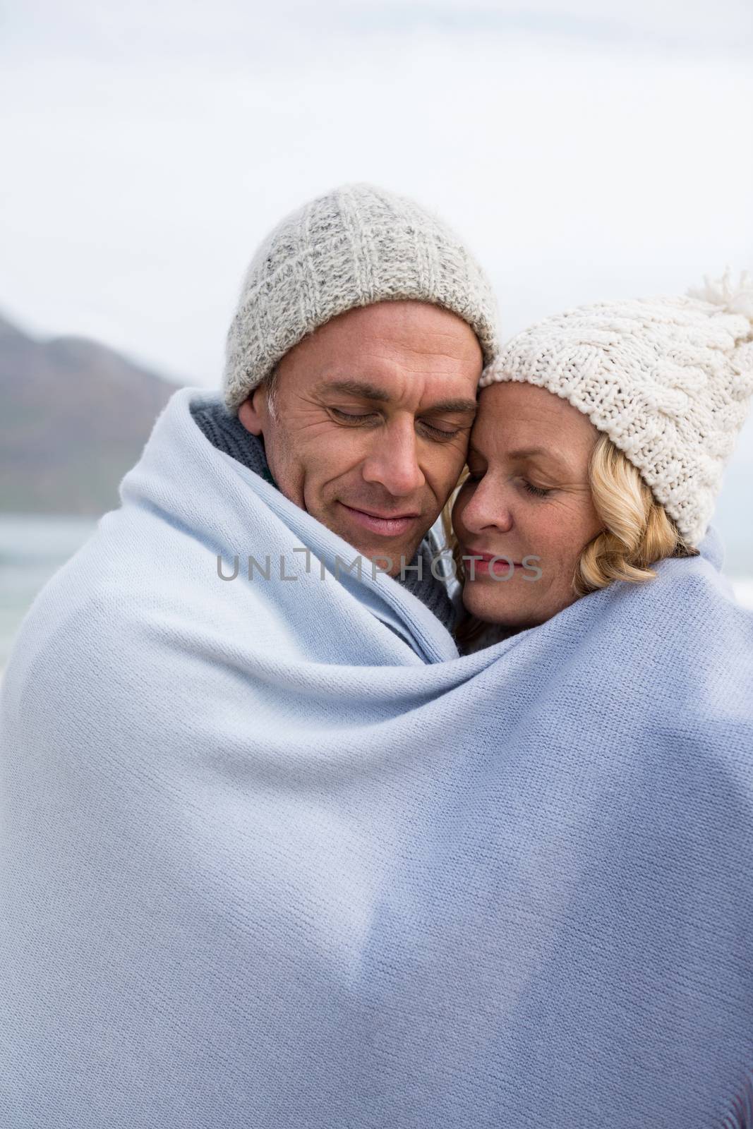 Mature couple wrapped in blanket on the beach by Wavebreakmedia