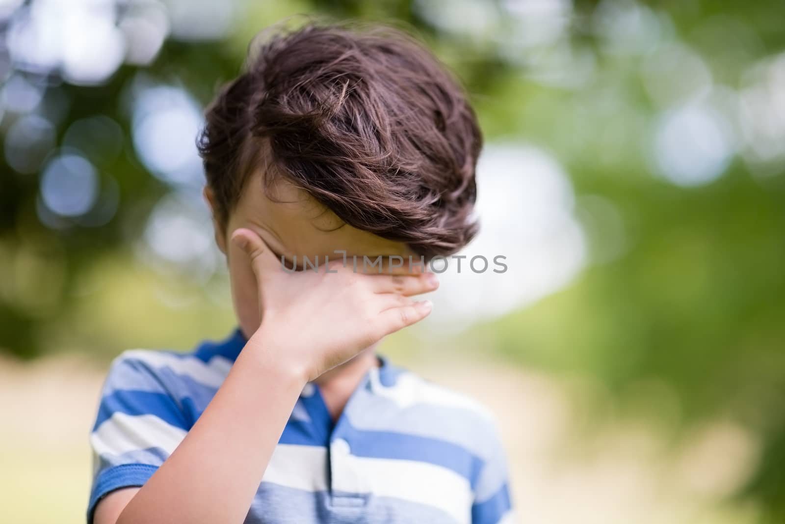 Boy covering eyes with hand in park on a sunny day