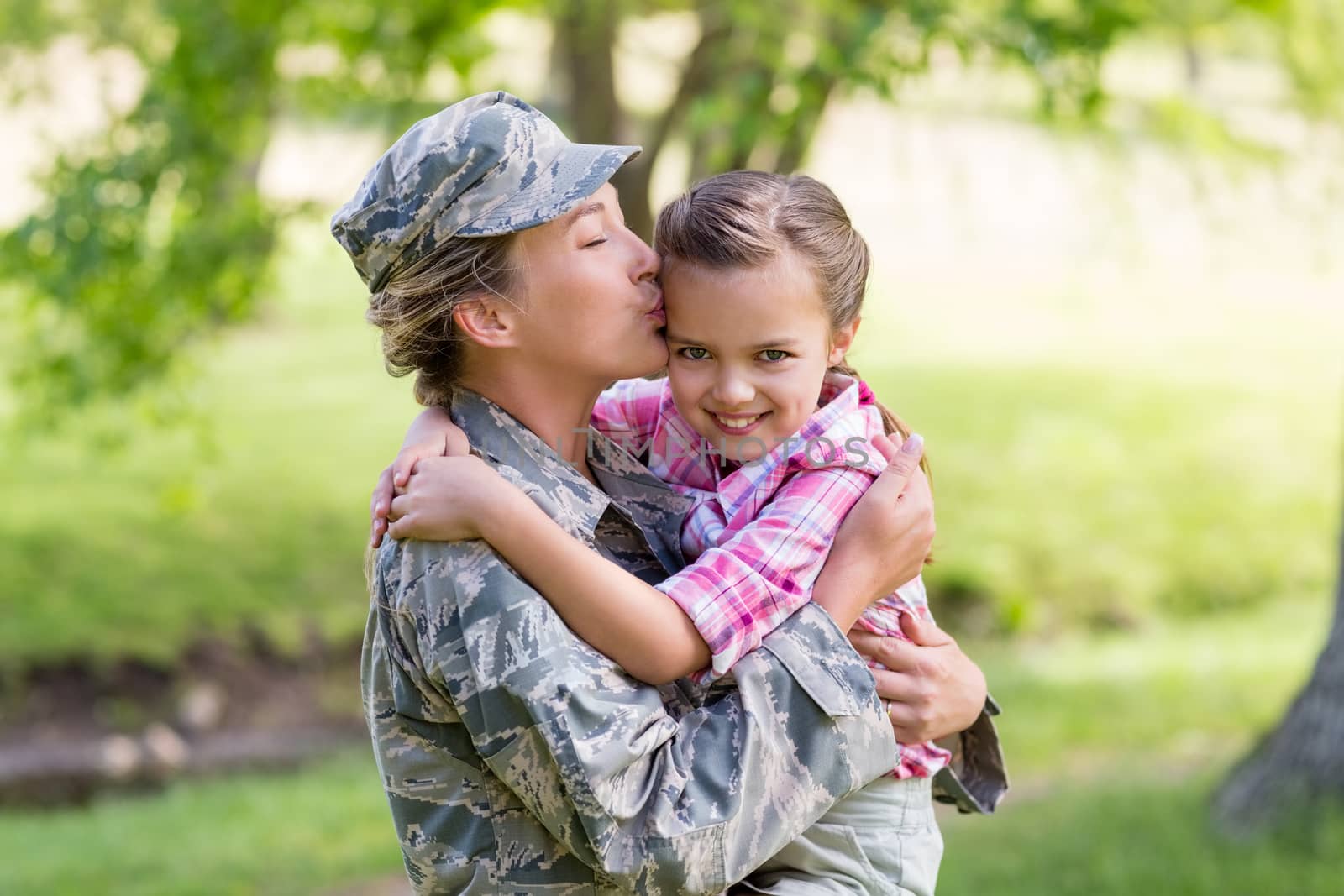 Happy female soldier kissing her daughter in park by Wavebreakmedia