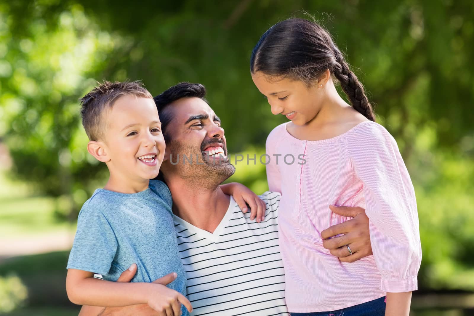 Father having fun with his son and daughter in park on a sunny day