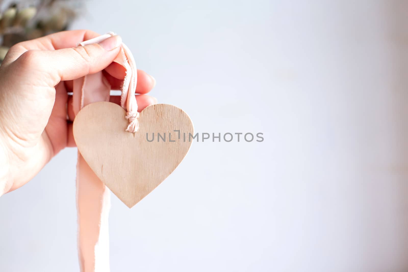 Light wooden heart on a silk pink ribbon. Hand holding a wooden heart pendant on a chiffon ribbon. Copy space.