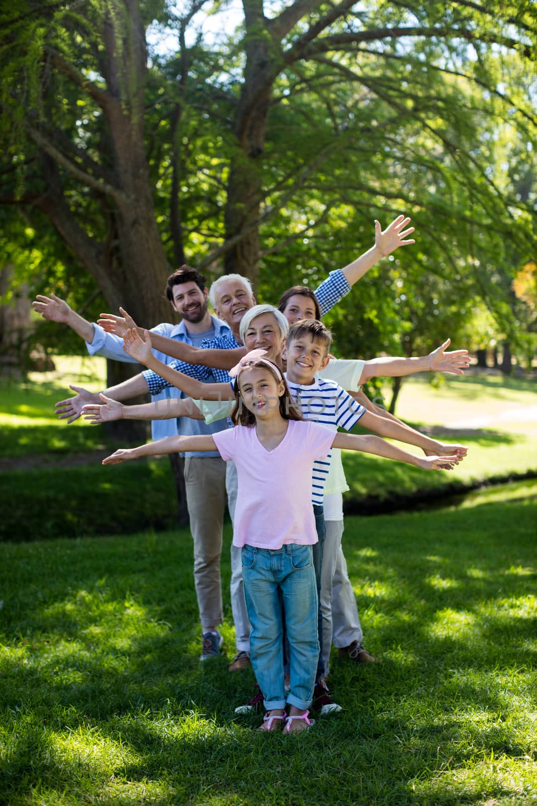 Multi generation family standing in a row with arms outstretched at park