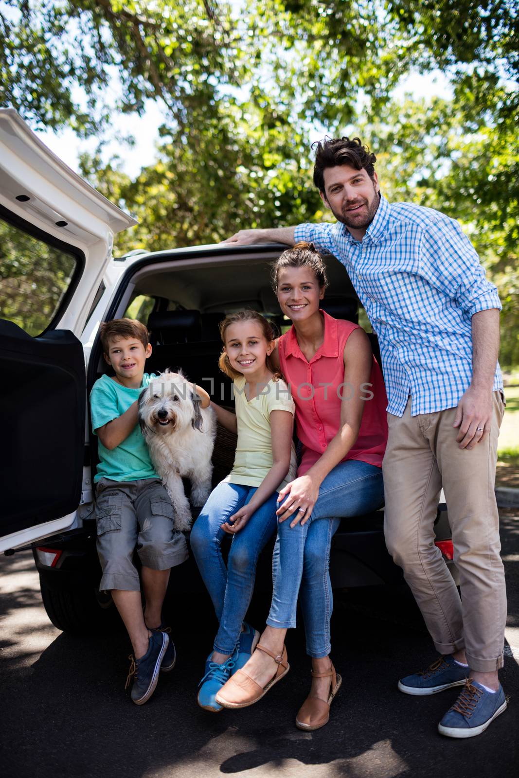 Portrait of happy family sitting in car trunk with their dog