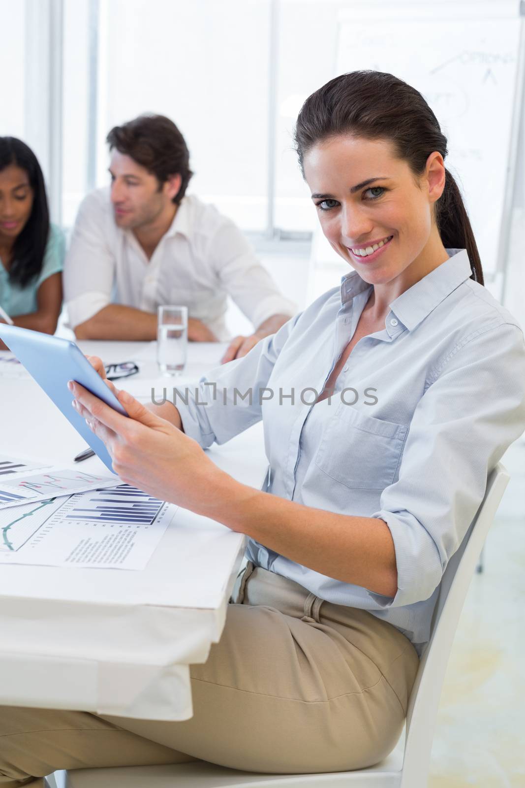 Attractive businesswoman using tablet while her coworkers are working hard behind her