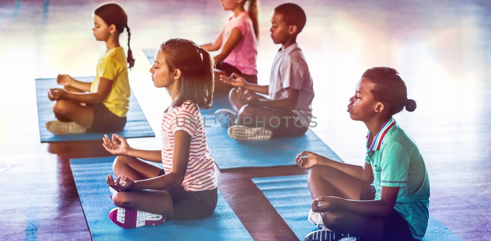 School kids meditating during yoga class in basketball court at school gym