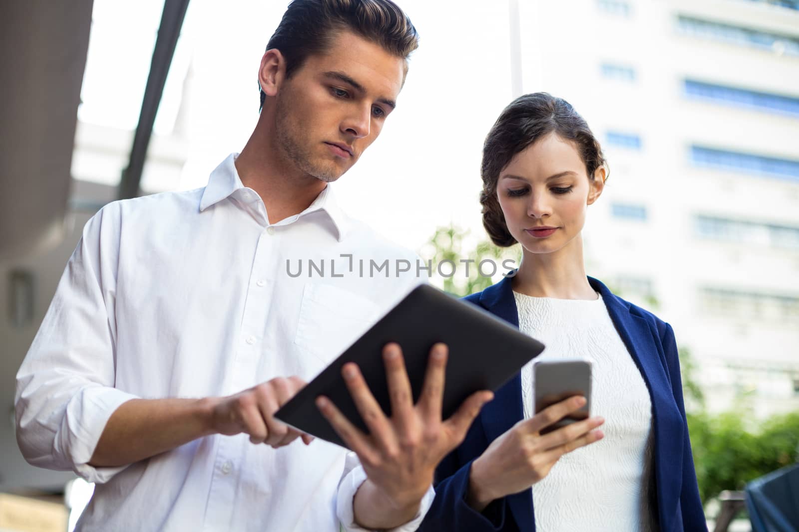 Businessman and woman using mobile phone and digital tablet by Wavebreakmedia