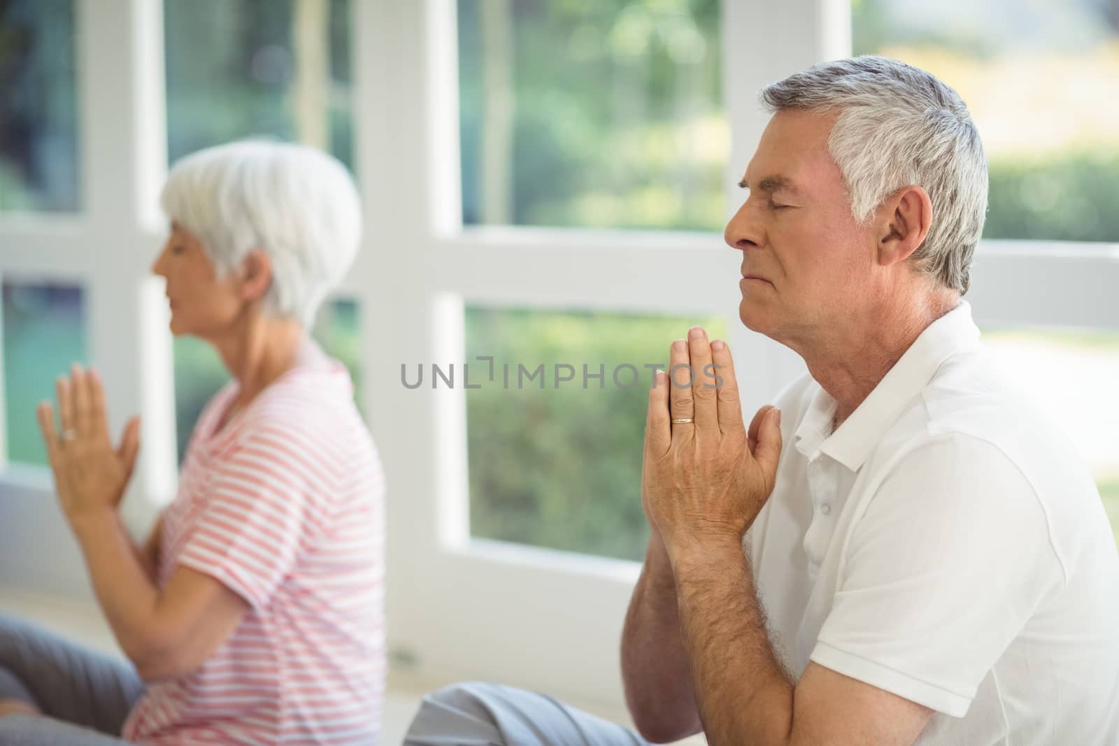 Senior couple performing yoga on exercise mat at home