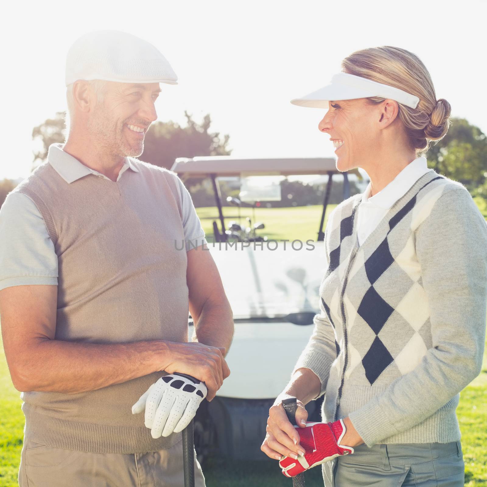 Happy golfing couple chatting with golf buggy behind by Wavebreakmedia