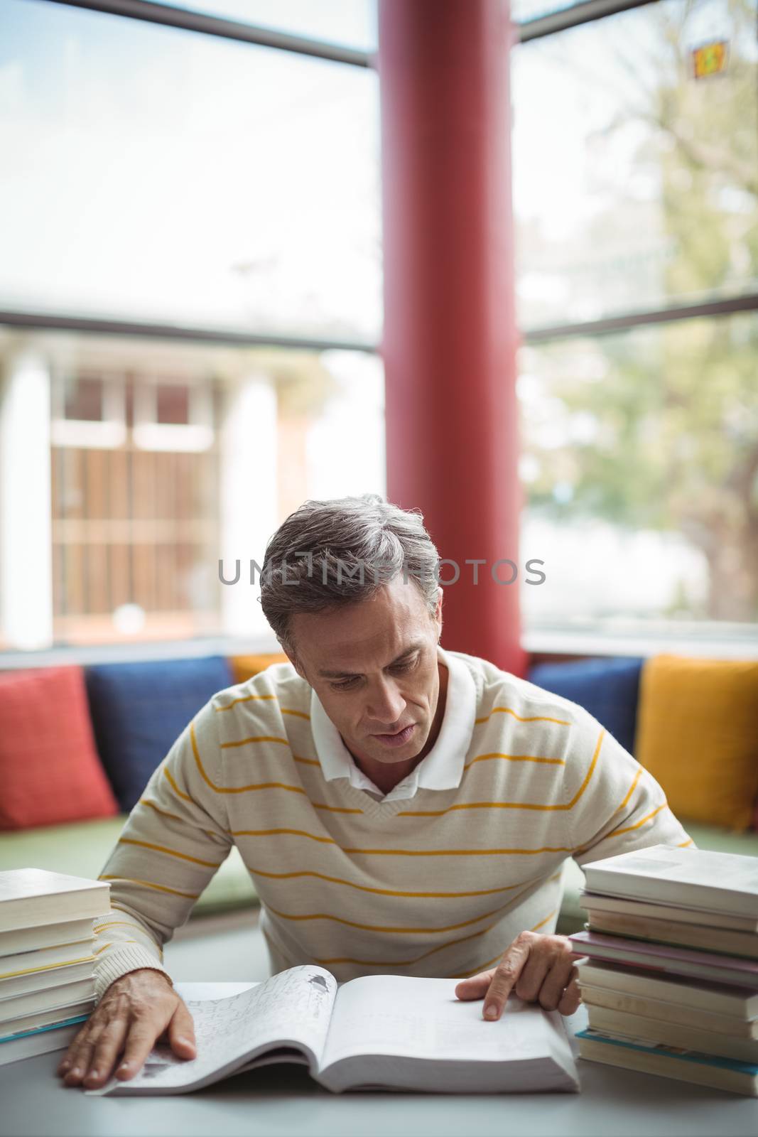 Attentive school teacher reading book in library by Wavebreakmedia