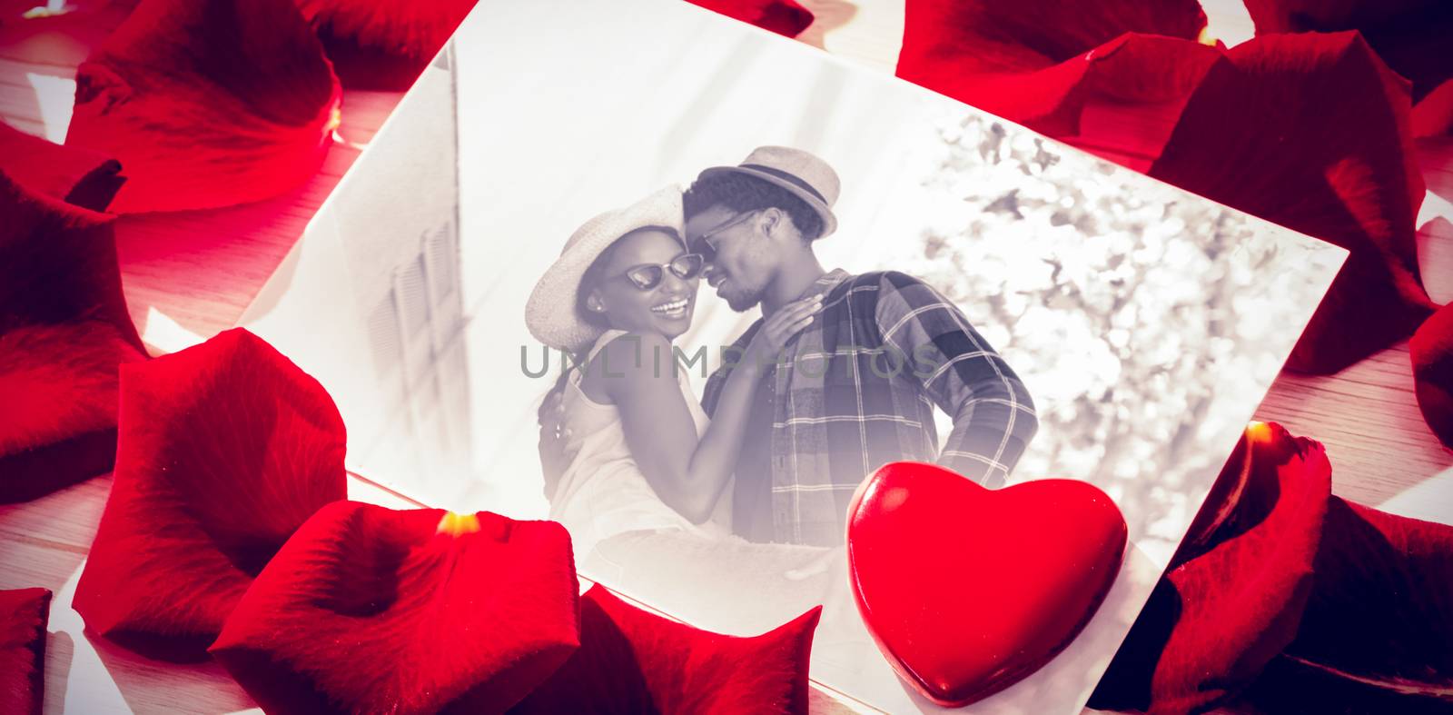 Card with red rose petals against romantic young couple dancing