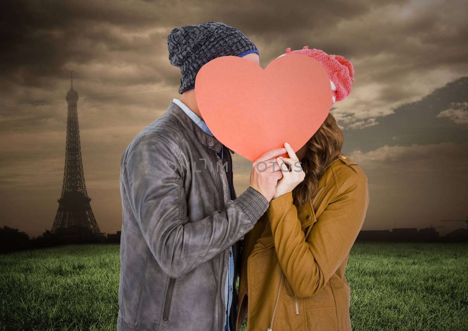 Couple hiding their face behind heart against digitally generated eiffel tower at distance