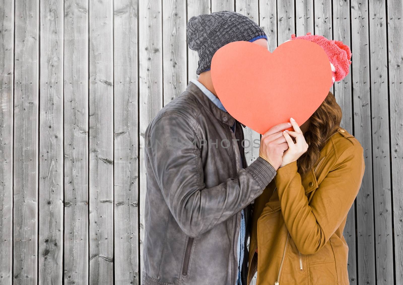 Romantic couple hiding their face behind heart against wooden background