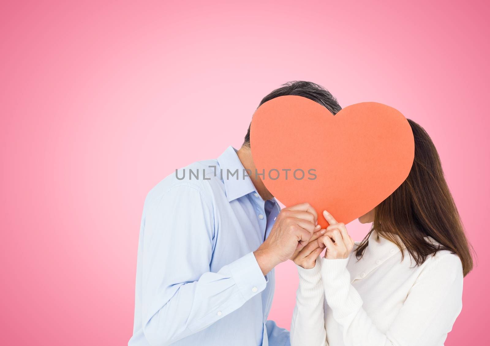 Romantic couple holding heart shape and kissing each other against pink background