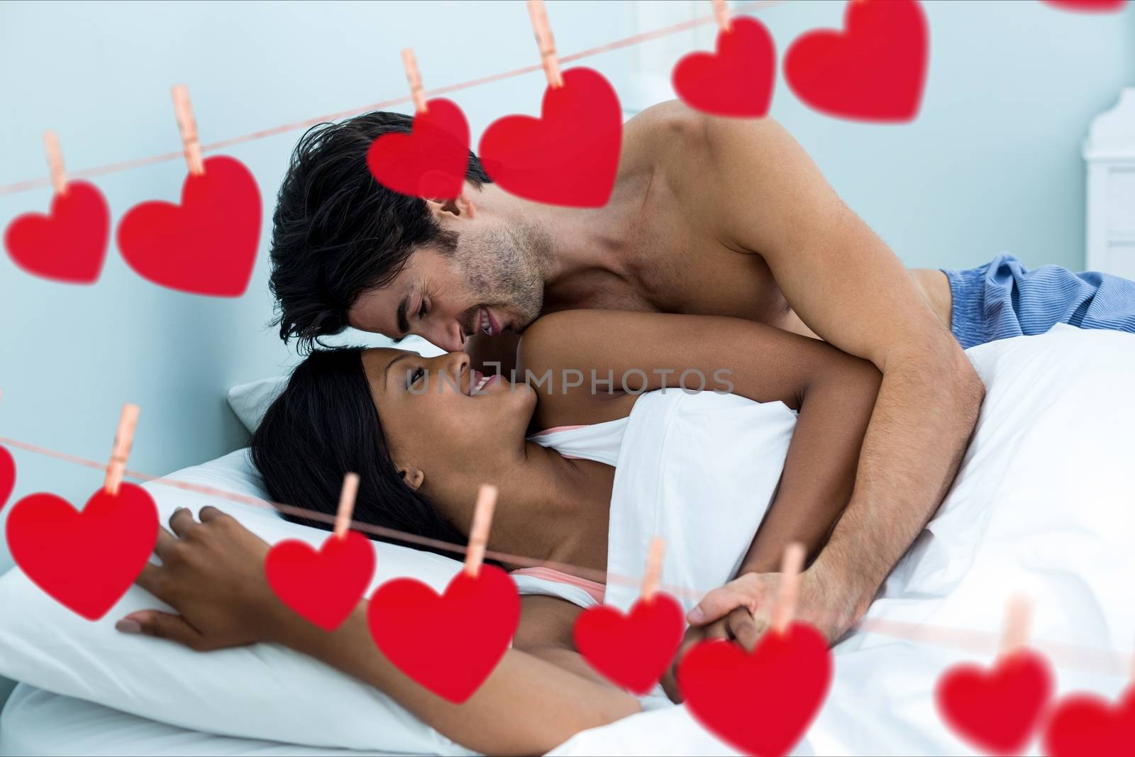 Composite image of red hanging hearts and young couple doing romance in bedroom at home