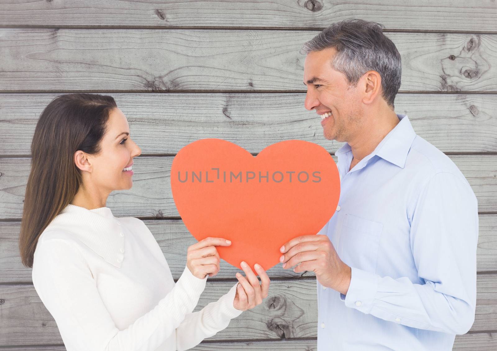 Romantic couple looking at each other and holding hearts against wooden background