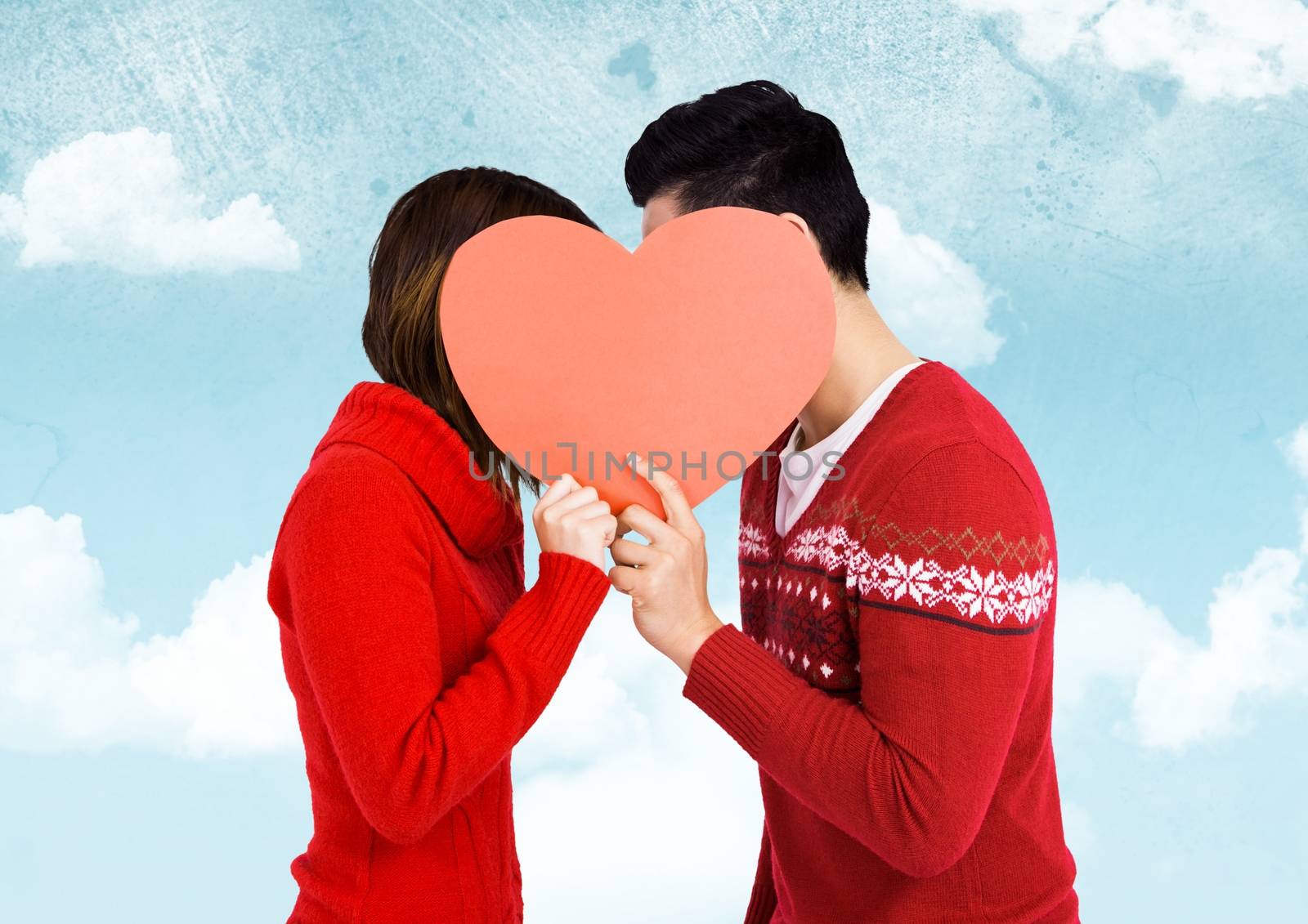 Romantic couple holding heart shape and kissing each other against sky