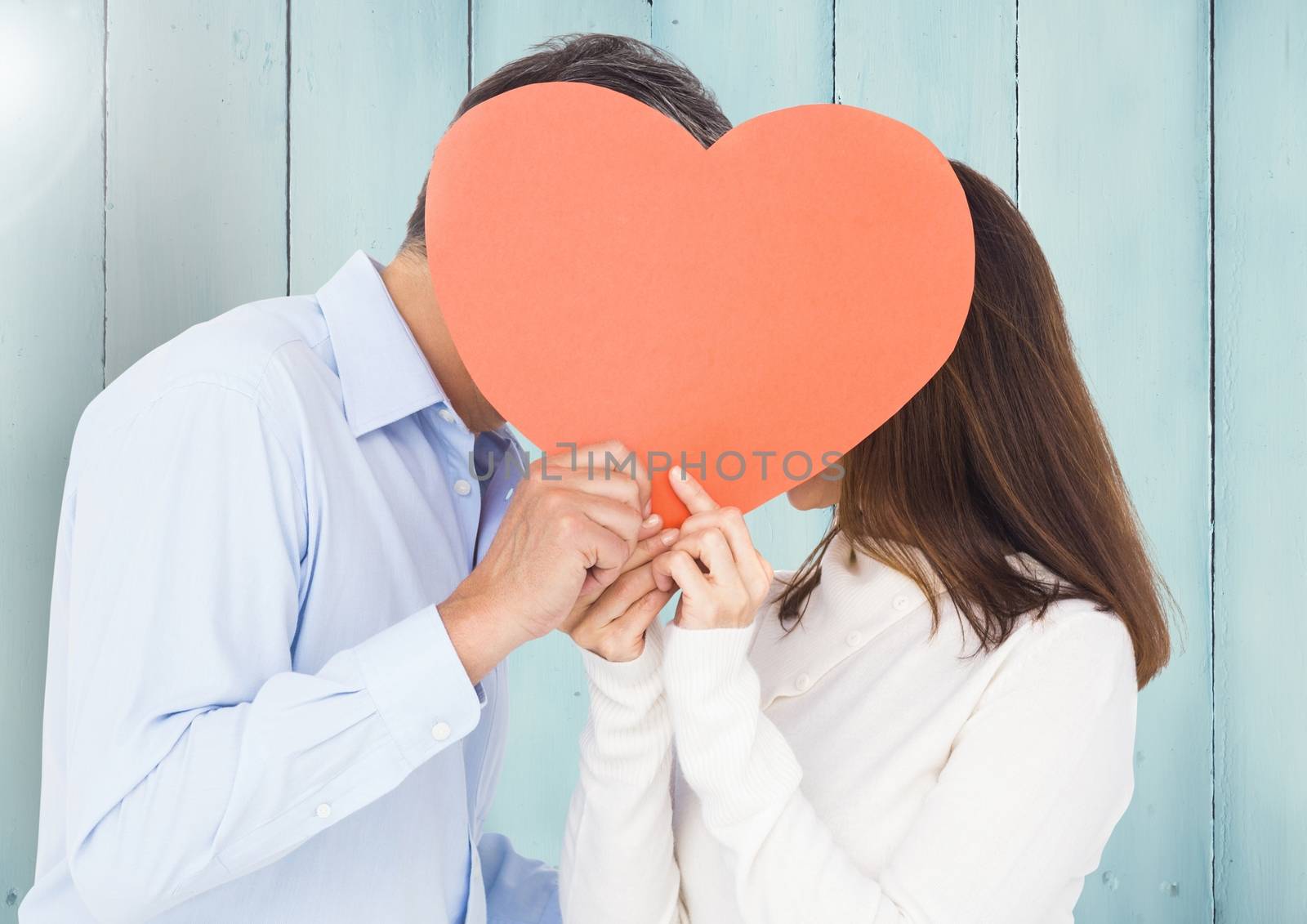 Romantic couple hiding their face behind heart against wooden background