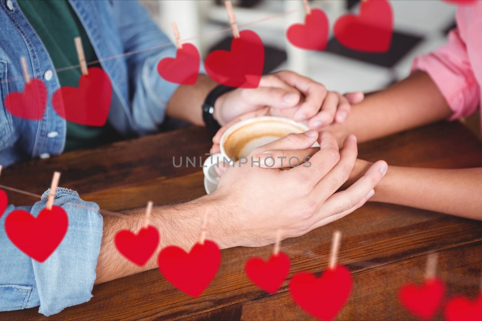 Mid section of romantic couple holding hands while having coffee