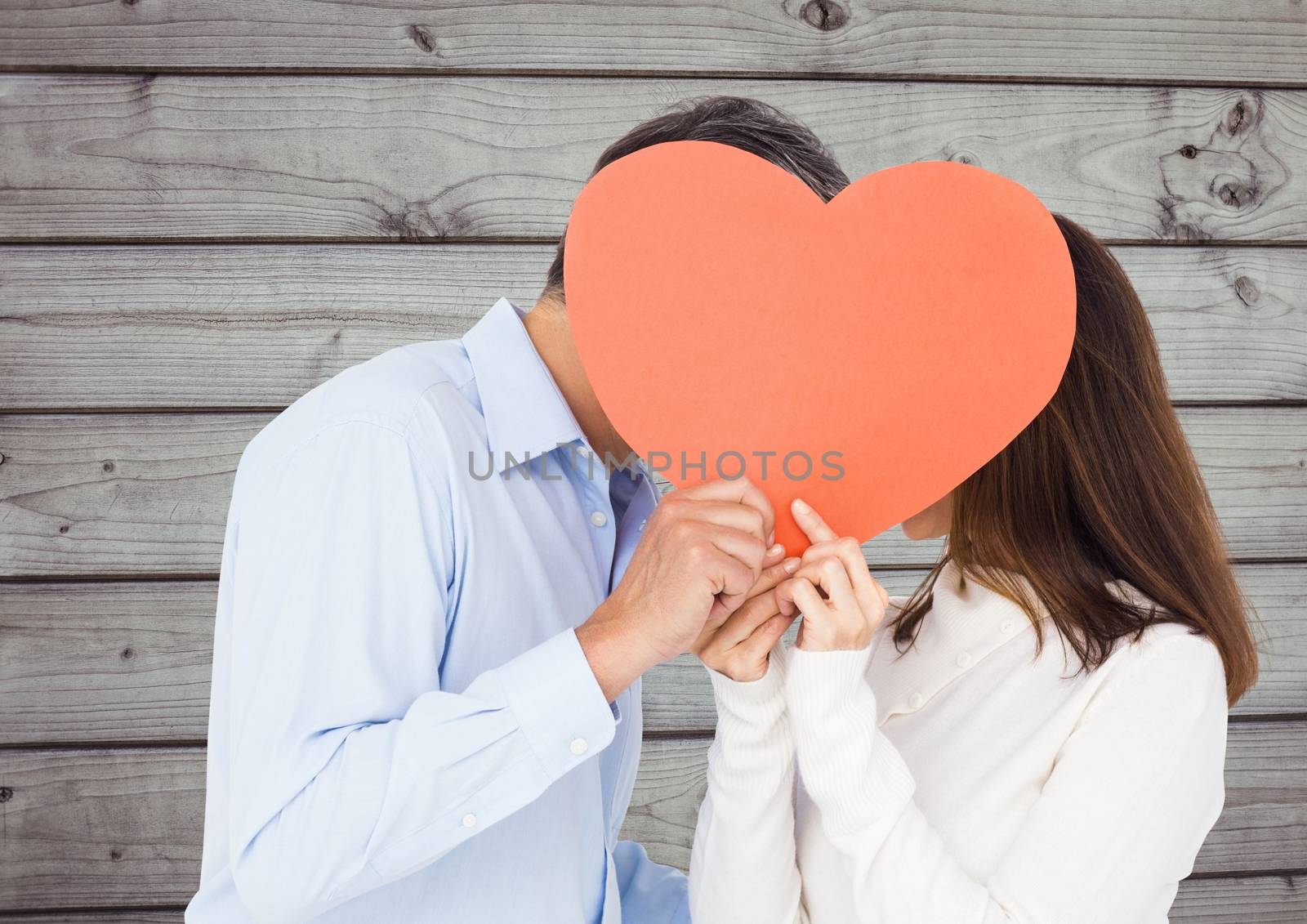 Romantic couple hiding their face behind heart against wooden background