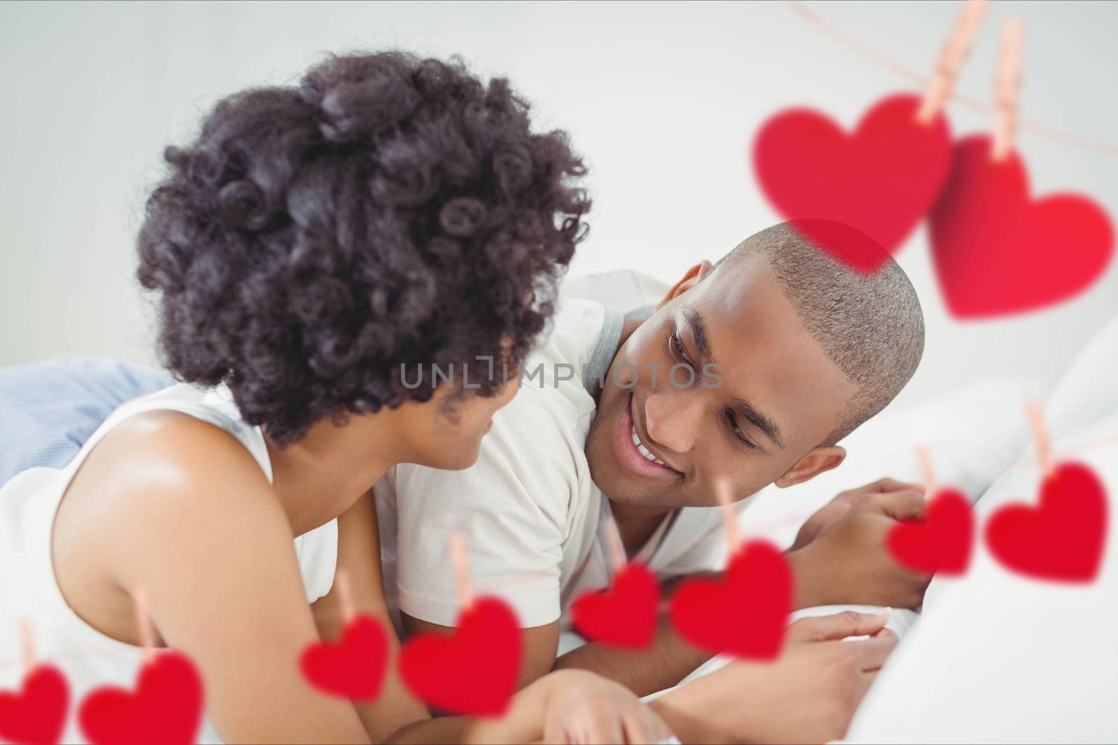 Composite image of red hearts and romantic couple lying on bed in bedroom at home