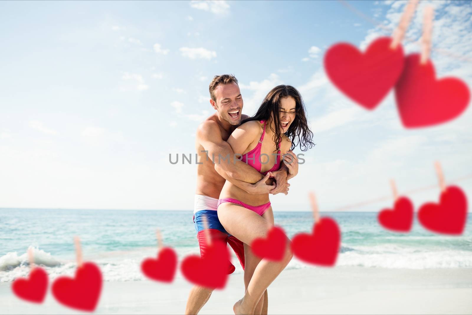 Romantic couple embracing each other on beach against hearts hanging on line