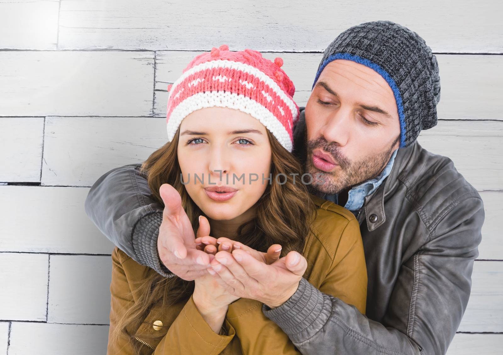 Romantic couple in winter clothing blowing snow against wooden background