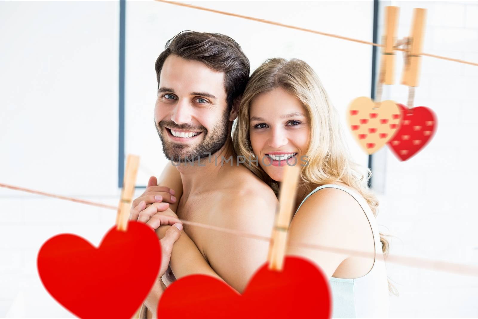 Composite image of romantic couple embracing with red hearts hanging on line