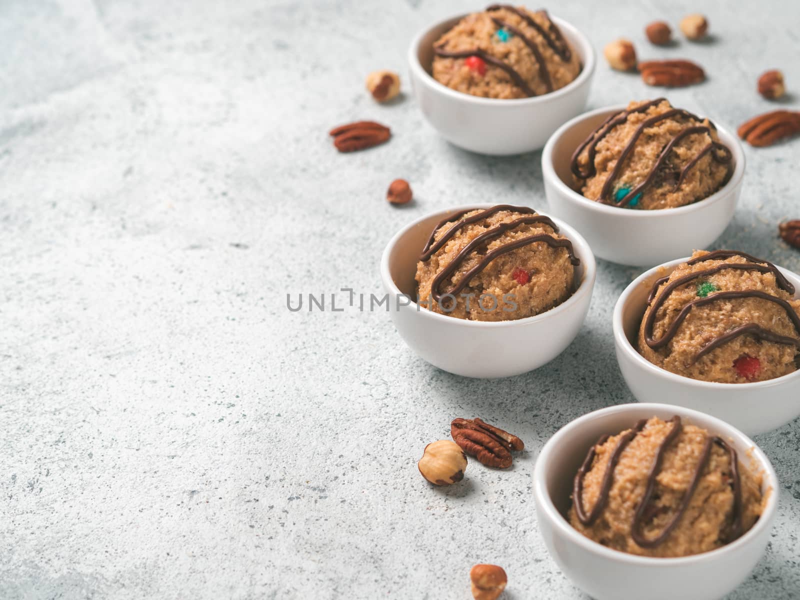 Safe-to-eat raw monster cookie dough in small portion bowl and nuts on gray cement background. Ideas and recipes for kids and toddlers meal. Copy space for text.