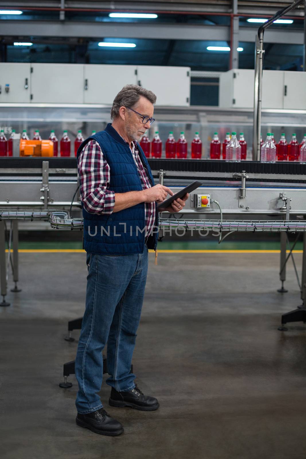 Factory worker using digital tablet next to production line in drinks production plant