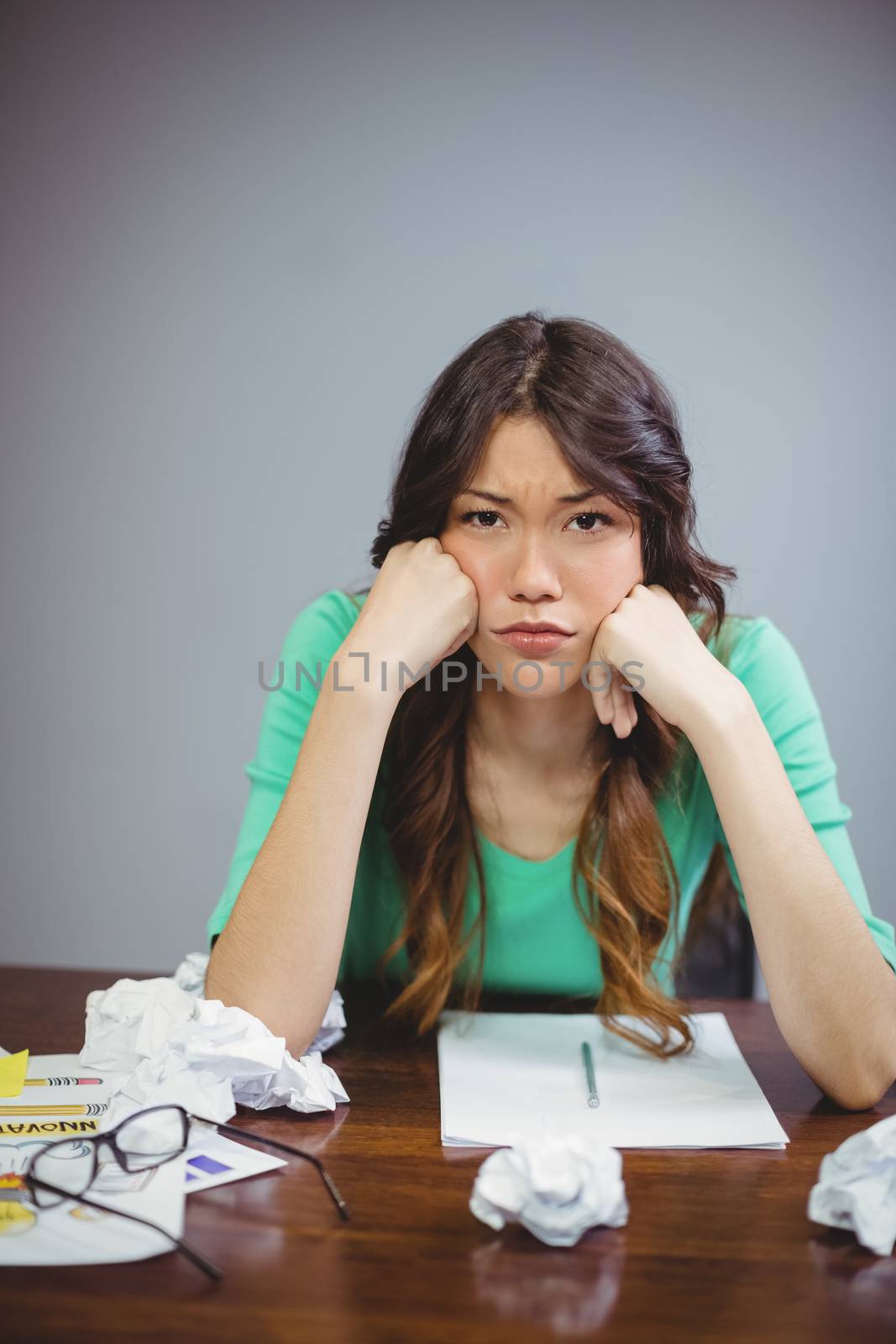 Frustrated female business executive sitting with crumpled paper balls in office