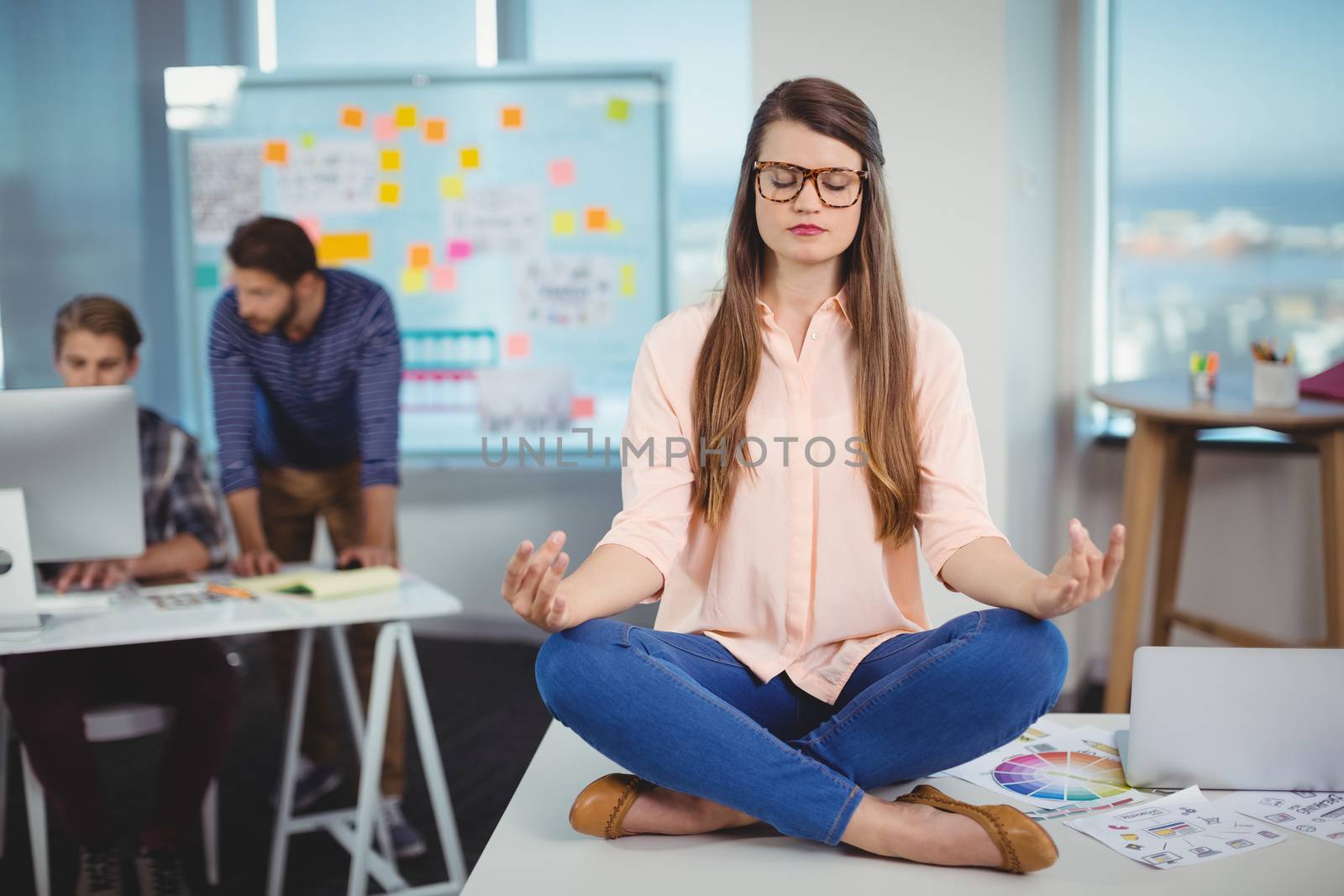 Female graphic designer sitting on table and meditating by Wavebreakmedia