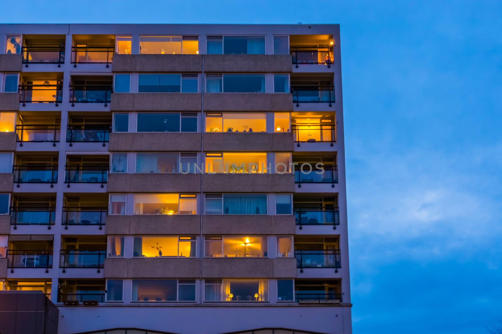 Apartments complex with lighted windows in the evening, modern city architecture in tilburg, The Netherlands by charlottebleijenberg