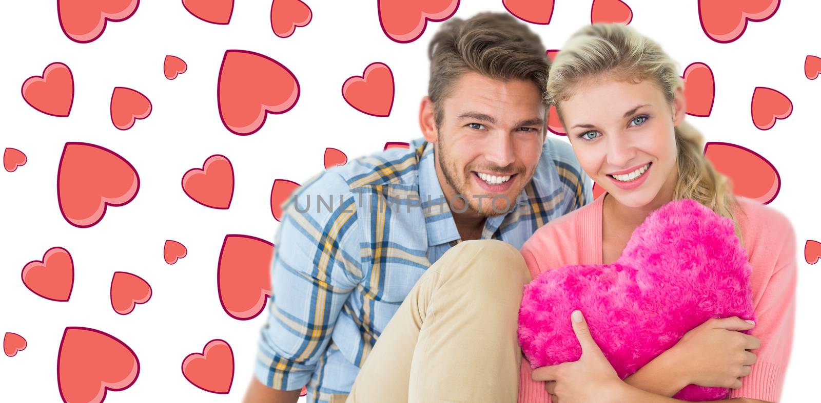Attractive young couple sitting holding heart cushion against background with hearts