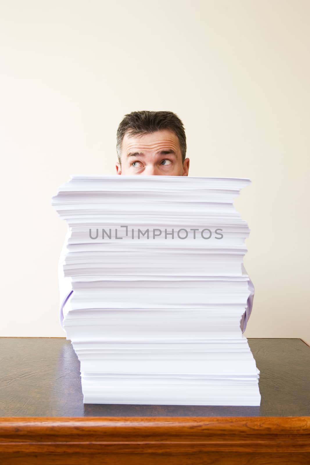 Caucasian businessman behind a stack of paper themes of overworked deadlines working late