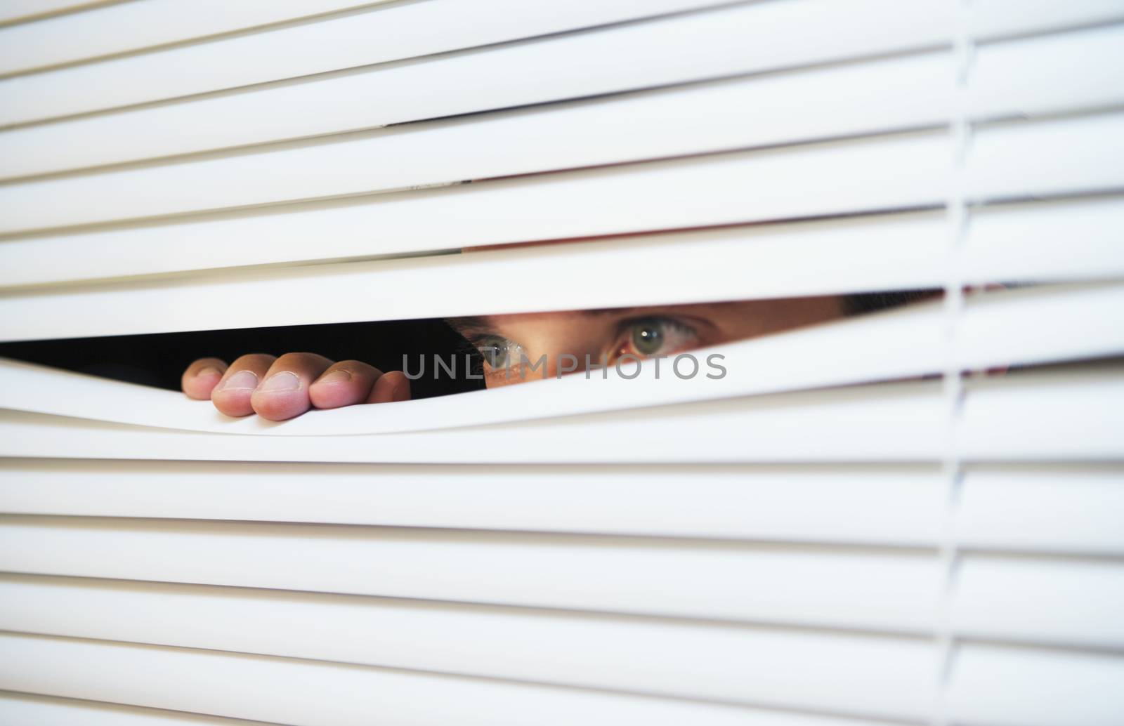 Caucasian man looking through the slats of a blind themes of curiosity watching surveillance