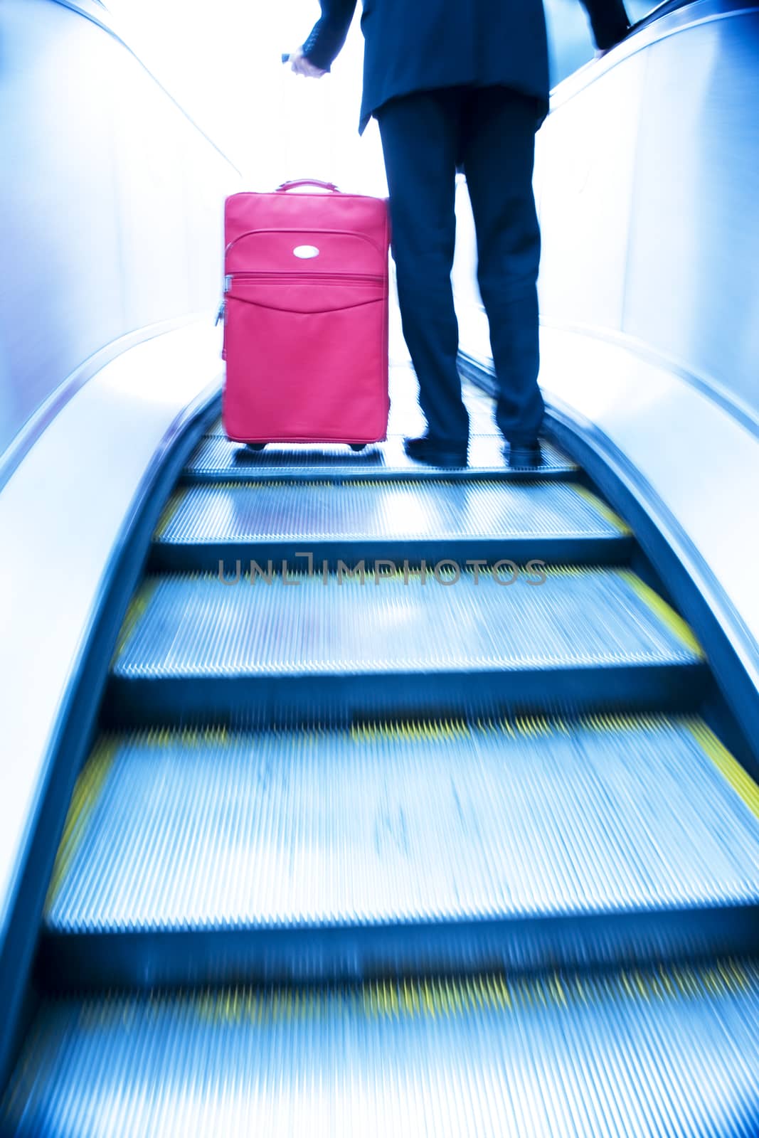 Businessman with suit case travelling up an escalator themes of departure travel deadlines arrival