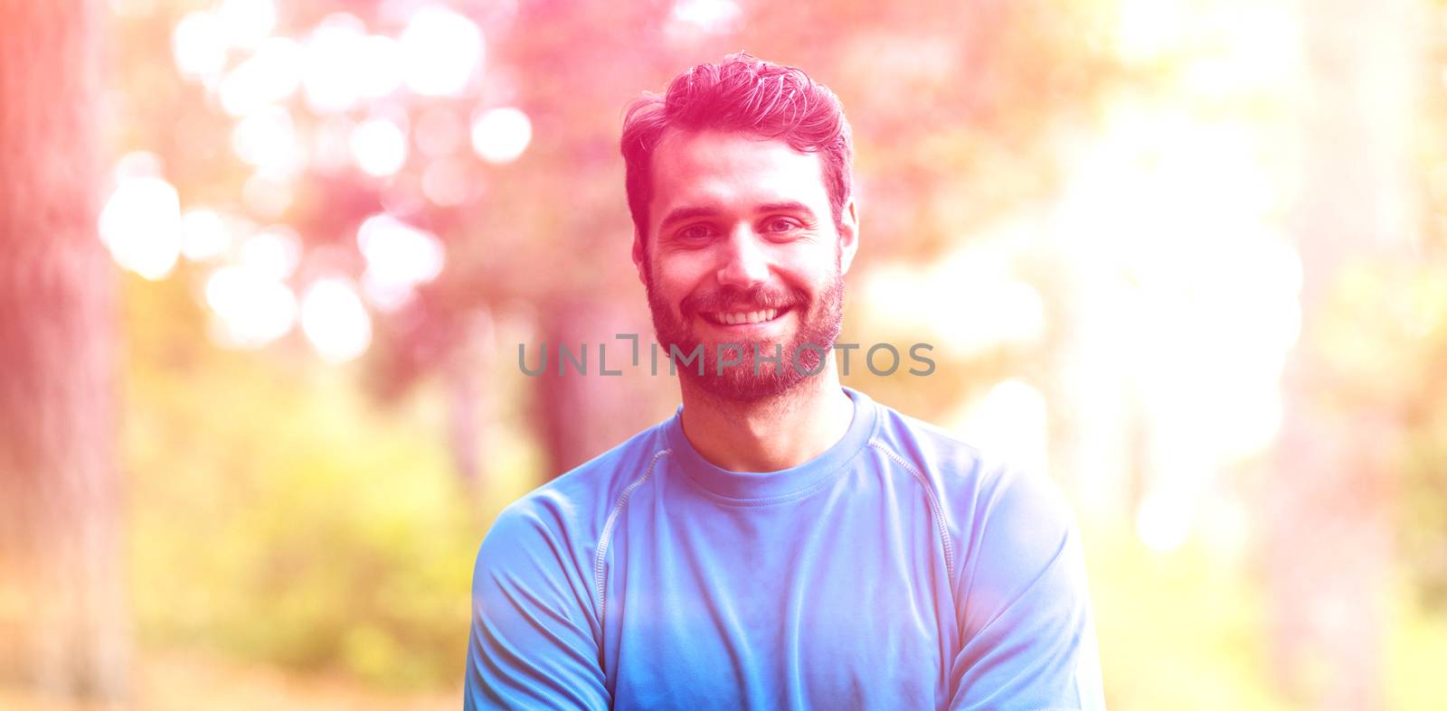 Portrait of smiling man standing in forest with arms crossed