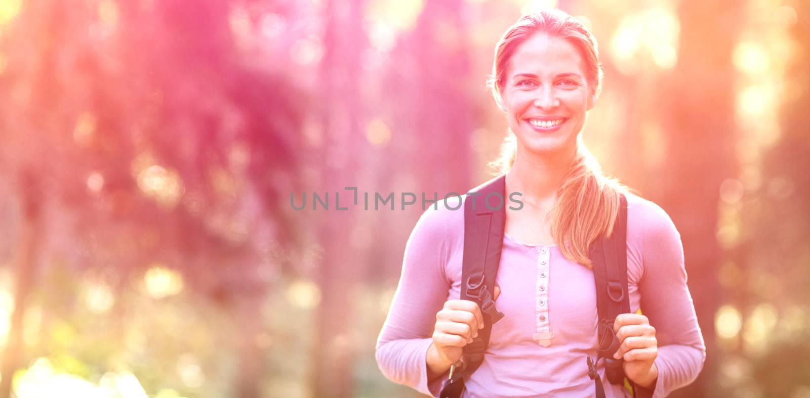 Portrait of smiling woman standing in forest carrying backpack by Wavebreakmedia