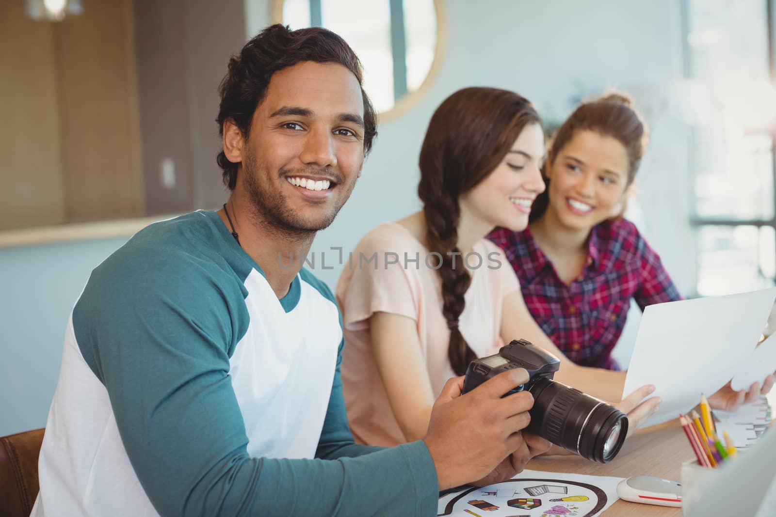 Portrait of fashion designer holding digital camera with colleagues in background in office