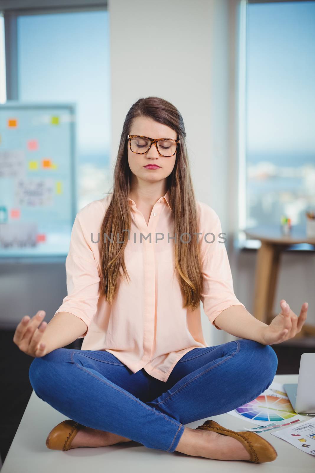 Female graphic designer sitting on table and meditating by Wavebreakmedia