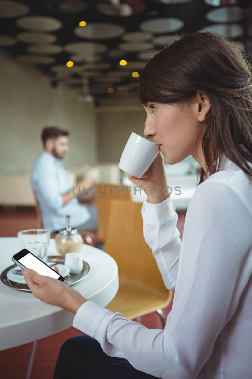 Thoughtful executive using mobile phone while having coffee in cafÃ©